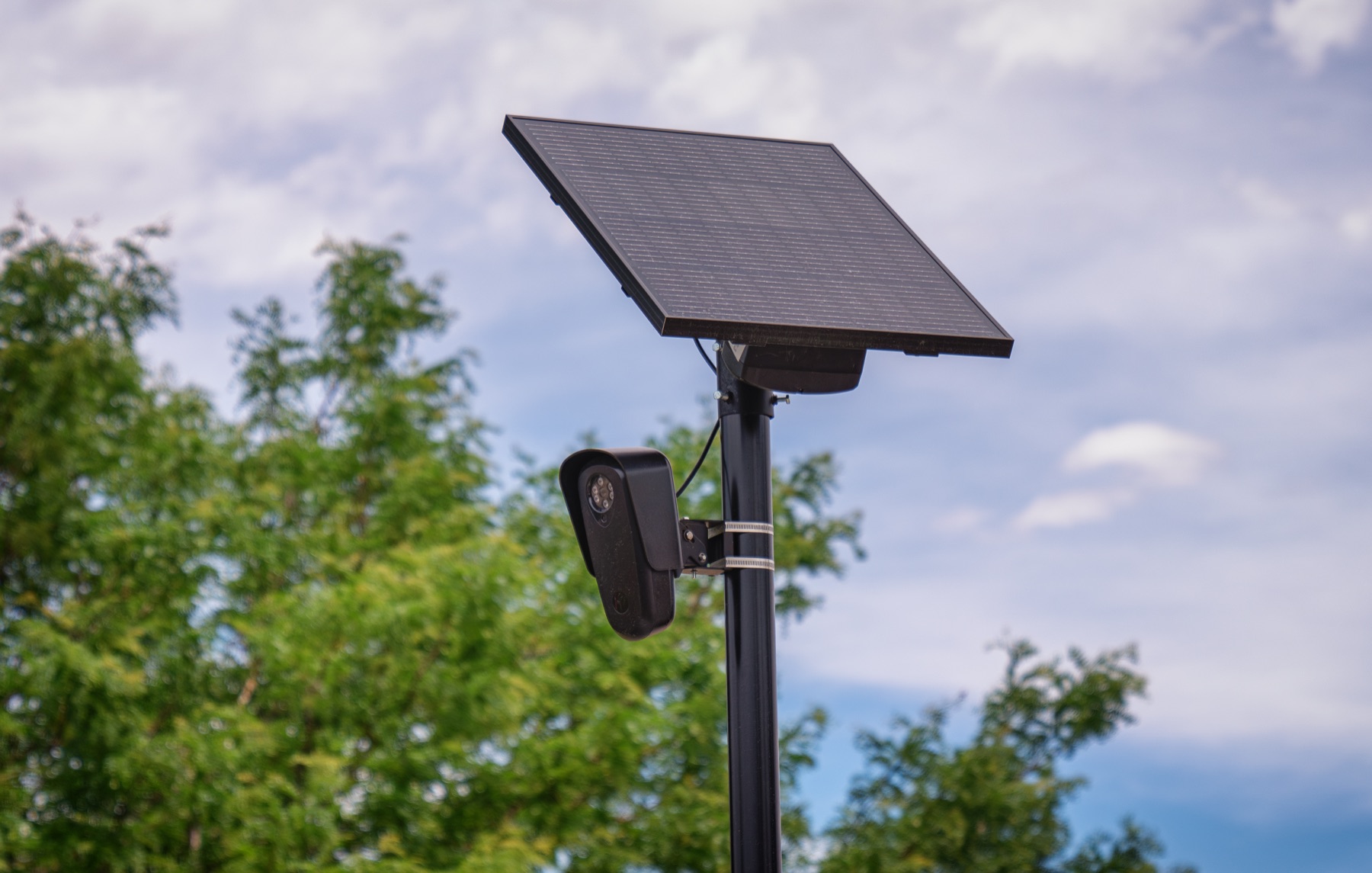 A Flock Safety automated license plate reader camera mounted beneath a solar panel against a blue sky.