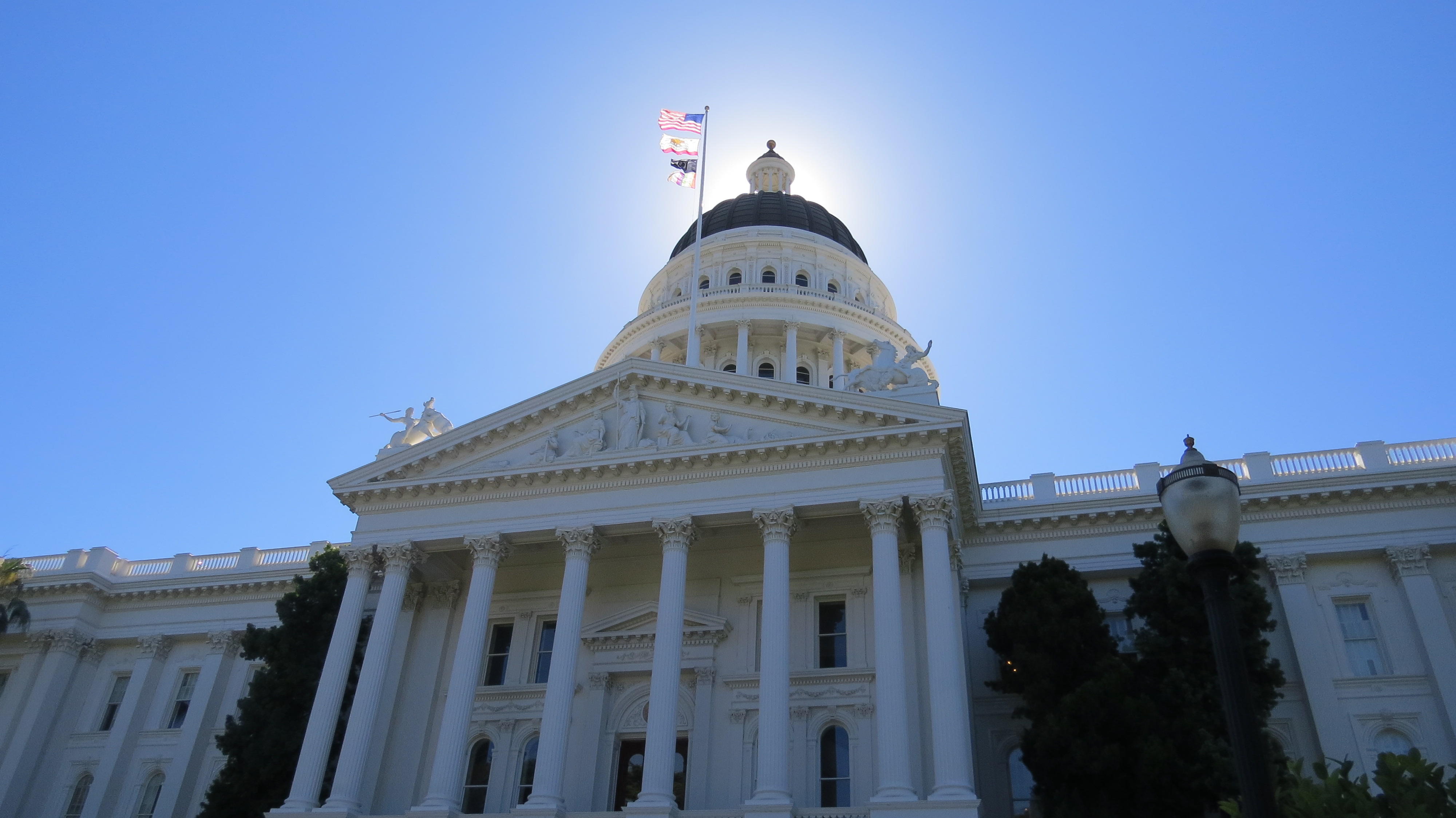 Low-angle view of the California State Capitol, its dome silhouetted against the morning sun.
