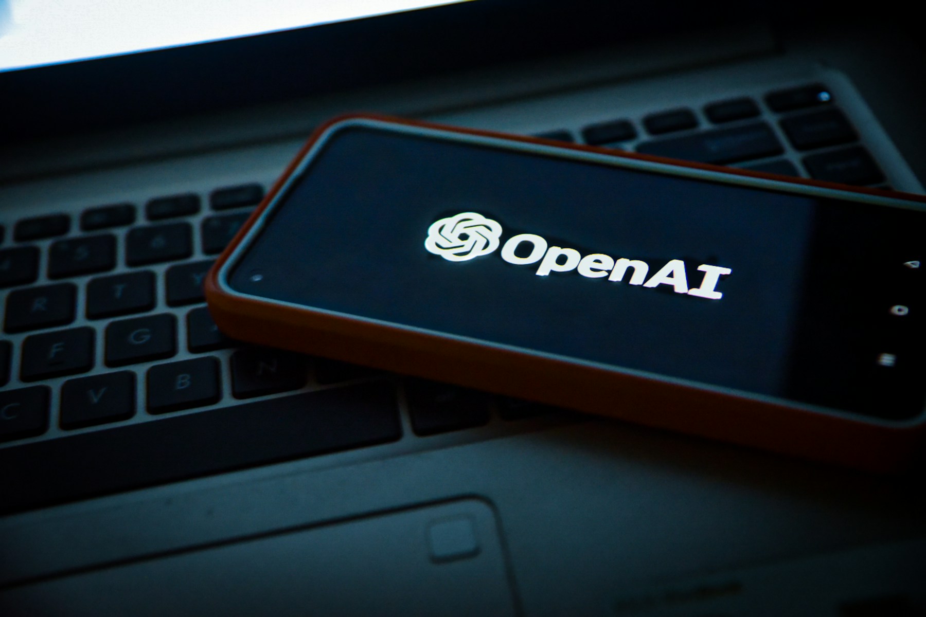 OpenAI logo on a phone resting across a laptop keyboard.