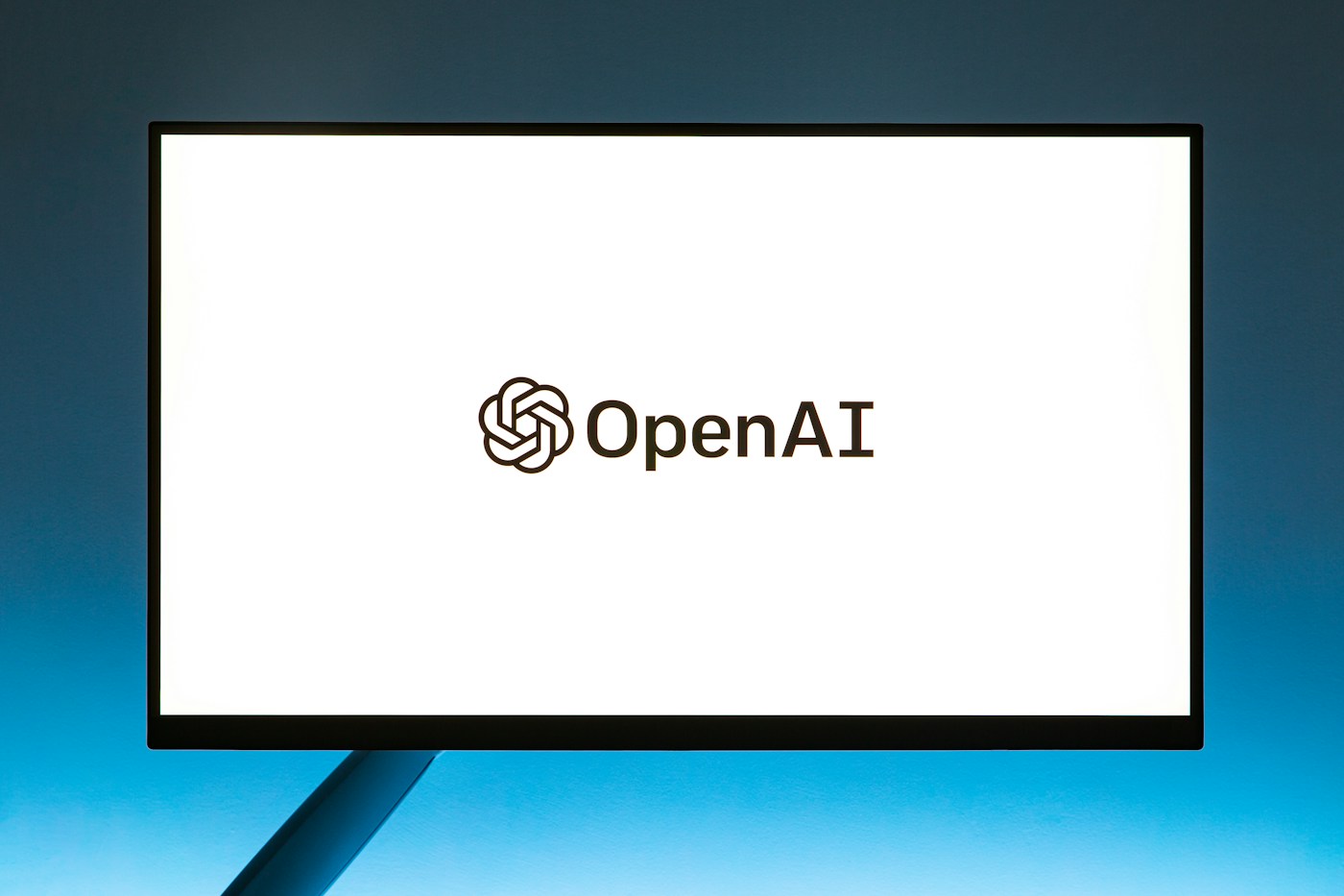 OpenAI’s logo on a bright monitor against a blue-lit background.