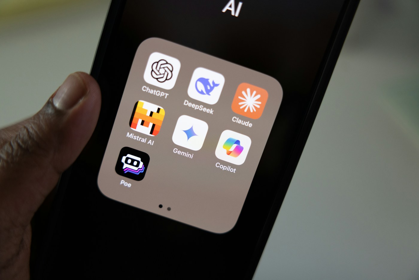 A hand holding a smartphone displaying AI app icons, including Claude.