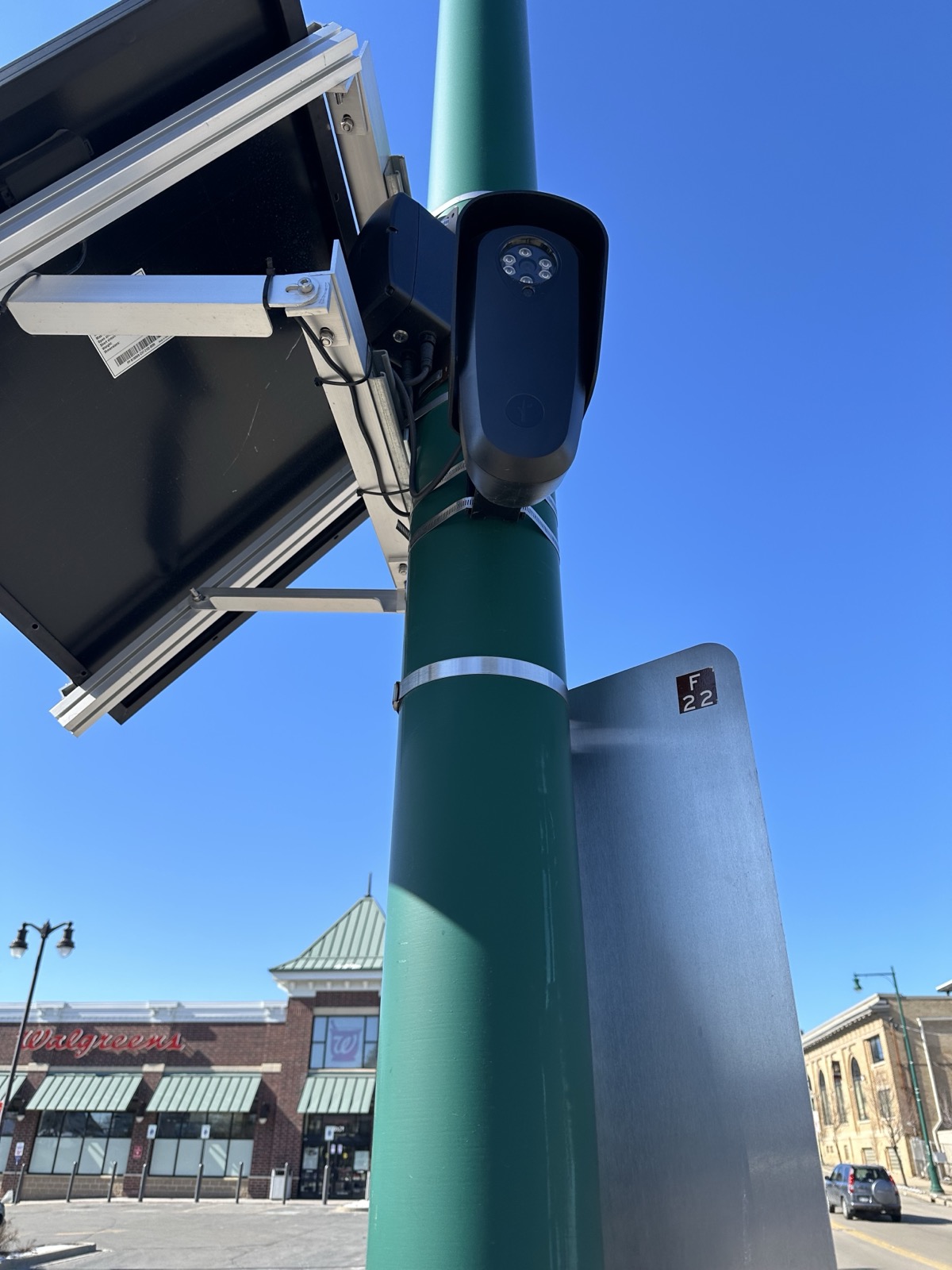 A Flock Safety license-plate reader mounted beneath a solar panel against a blue sky.
