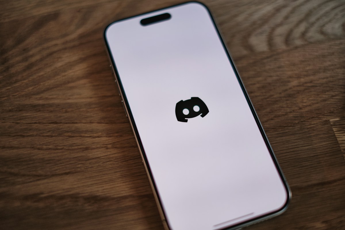 A phone displaying the Discord logo on a wooden table.